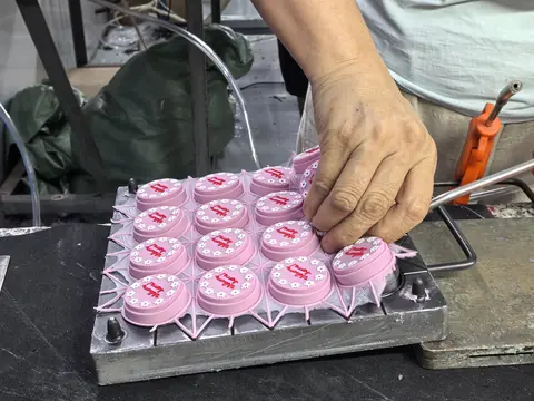 A bare hand lifting a freshly demoulded pink silicone part from a multi-cavity aluminium mould.